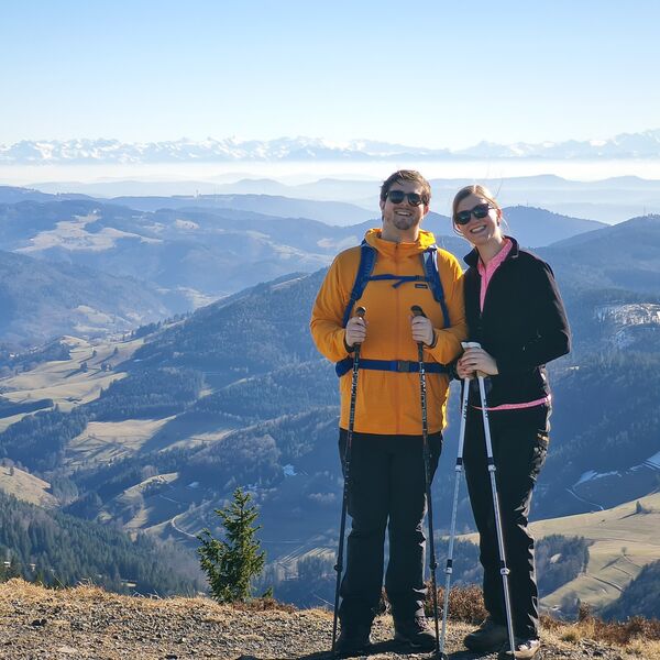 Mann mit orangenem Anorak und eine Frau mit schwarzer Jacke, beide mit Laufstöcken beim Wandern auf dem Belchen